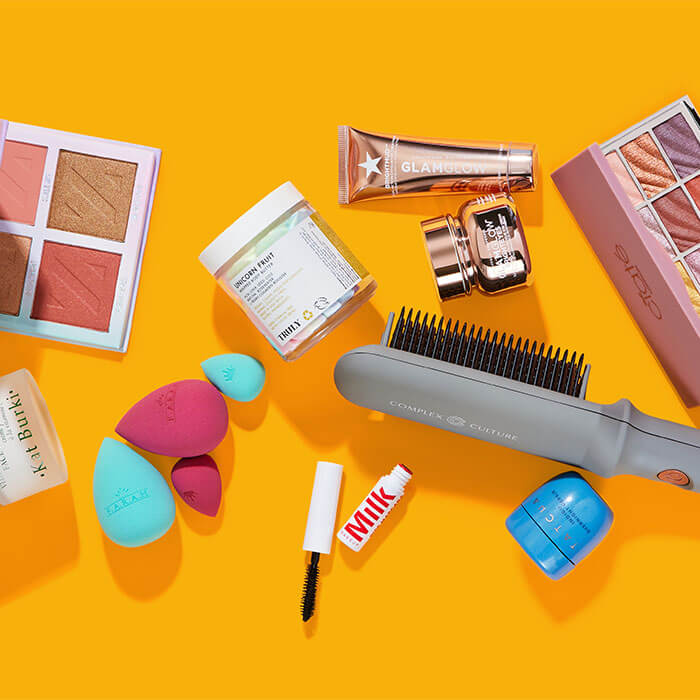 Beauty and makeup products from various brands scattered on bright orange background