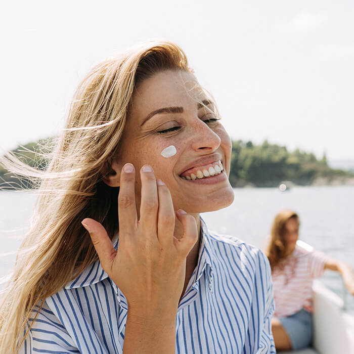 Photo of a smiling woman applying sunscreen while taking a boat ride with her friend