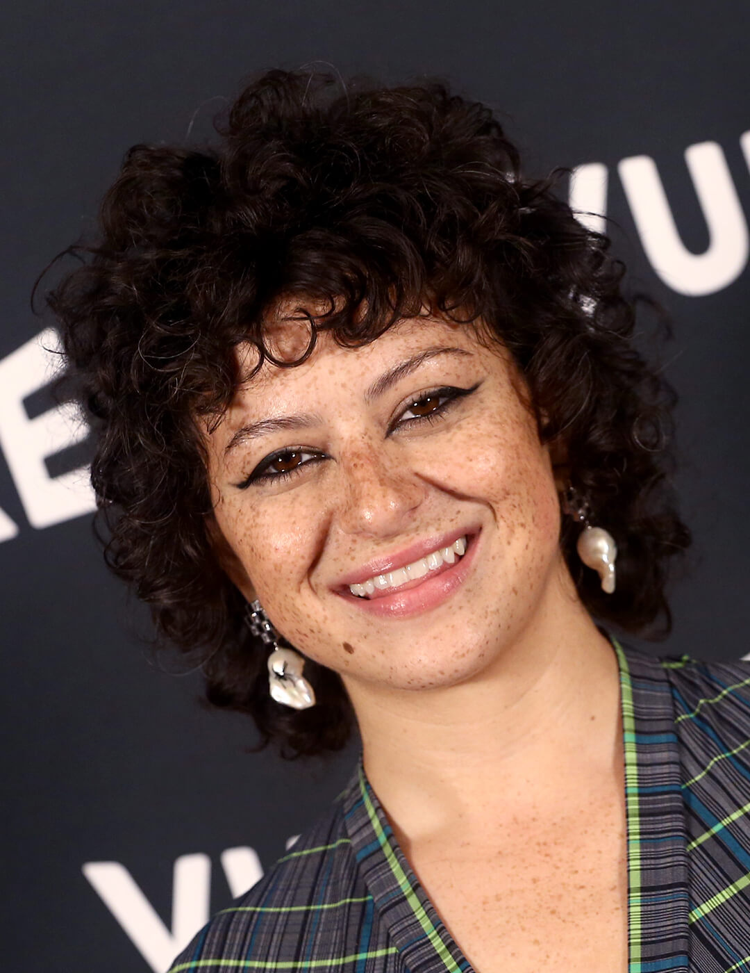Smiling Alia Shawkat rocking a short curly hairstyle with wispy bangs
