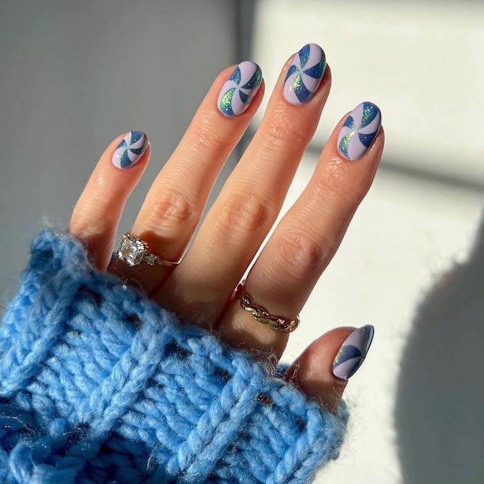 A close-up image captures a woman's hand adorned with vibrant blue candy cane-inspired festive nail art, complemented by an exquisite gold and diamond ring