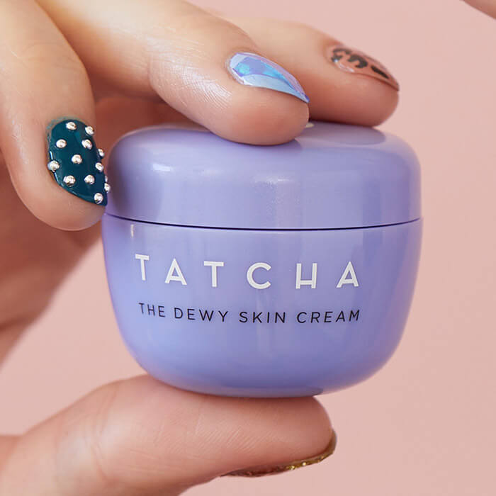 Close-up of a model's hand with bedazzled nail art holding the TATCHA The Dewy Skin Cream