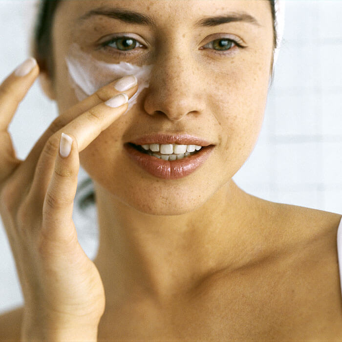 A woman who has recently taken a bath and  gently applying moisturizer beneath her eye