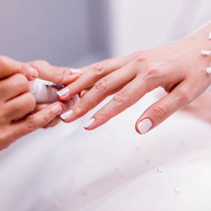 A closeup photo of someone applying a coat of pearly white nail polish to a bride's hand